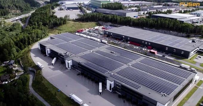 Solcellepanel på taket av et stort næringsbygg, sett fra luften.